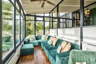 a screened in porch with green furniture and windows at Caer Beris Manor By Group Retreats in Builth Wells