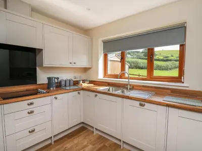 a kitchen with white cabinets and a sink and a window at Awel y Bryn in Rhayader