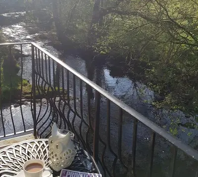 a table with a tea pot on a balcony with a river at River Cottage Brecon: Hot Tub, Fire, Balcony, Wifi in Brecon