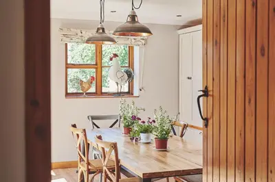 a dining room with a table and a chicken in a window at Powk Meadow Farmhouse in Leominster