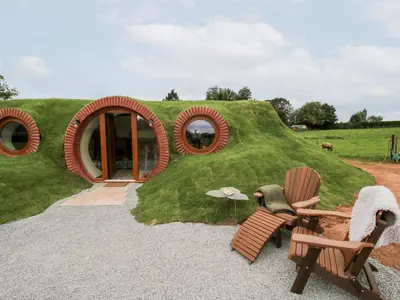 a house with a grassy hill with two chairs and a table at Shire's End in Caynham