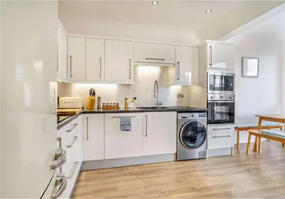a kitchen with white cabinets and a washer and dryer at No.1 Sail House in New Quay