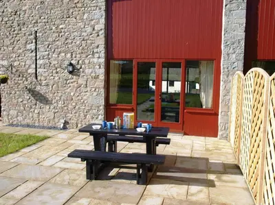 a picnic table in front of a building with a red door at Peregrine Stable Cottage in Llandovery