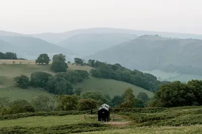 a black barn on a hill with mountains in the background at Hoku in Llangollen