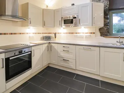 a kitchen with white cabinets and a sink and a stove at The Barn by Lyons in Talybont