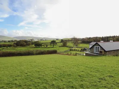 a farmhouse in a field with a large green field at Bryn Eglwys Cottage in Tywyn