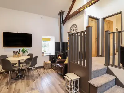 a living room with a staircase and a table and chairs at Bryn Eglwys Barn in Tywyn