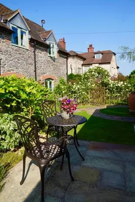 a table and a chair with flowers on a patio at Nest Holiday Hideaway Wren Cottage-Beautiful Location in the Long Mynd Area of Outstanding Natural Beauty- WHIRLPOOL JACUZZI BATH! in Picklescott