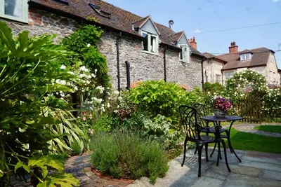 a garden with a table and chairs in front of a house at Nest Holiday Hideaway Wren Cottage-Beautiful Location in the Long Mynd Area of Outstanding Natural Beauty- WHIRLPOOL JACUZZI BATH! in Picklescott