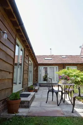 a patio with a table and chairs in front of a house at Nest Holiday Hideaway Wren Cottage-Beautiful Location in the Long Mynd Area of Outstanding Natural Beauty- WHIRLPOOL JACUZZI BATH! in Picklescott