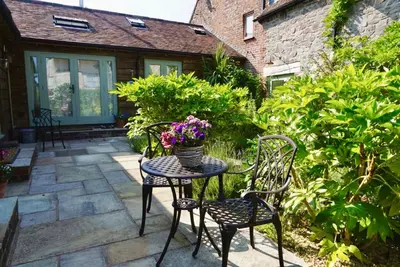 a patio table with chairs and a vase of flowers at Nest Holiday Hideaway Wren Cottage-Beautiful Location in the Long Mynd Area of Outstanding Natural Beauty- WHIRLPOOL JACUZZI BATH! in Picklescott