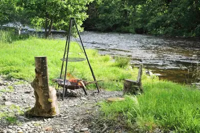 a grill next to a river with a tree stump at The Boatshed at Camp Plas in Welshpool