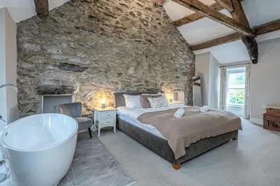 a bedroom with a stone wall and a bed and a bath tub at Ty Mawr Llanfair in Llanfair