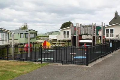 a playground behind a black fence in front of houses at Caravan 521 shuker Barmouth in Talybont
