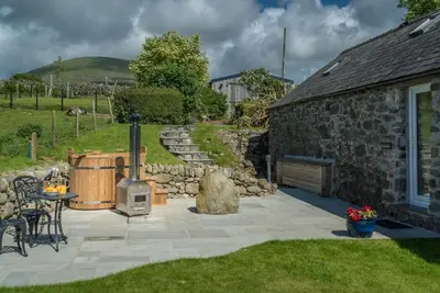 a patio with a stone building and a grill at Melin-Byrdir in Dyffryn