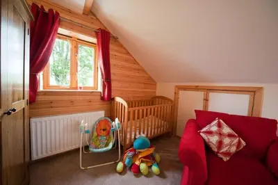 a nursery with a red couch and a baby crib at Beech Tree Eco Lodge in Brecon