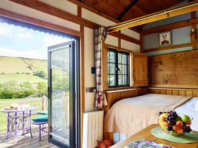a bedroom with a bed and a balcony with a table at The Flying Scotsman Shepherd's Hut with Hot Tub in Brecon