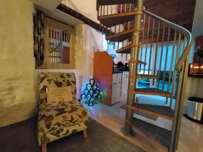 a living room with a spiral staircase and a chair at Yr Hen Efail - Quirky Old Smithy cottage near forest walks, cycling & lakes in Garthbeibio