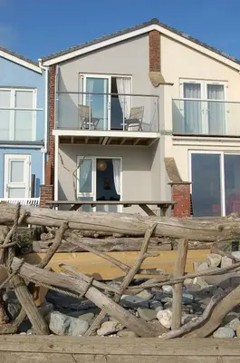 a house with a wooden fence in front of it at Chwerthin Y Mor Beach House in Tywyn