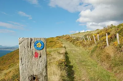 a wooden fence on a hill with a sign on it at Chwerthin Y Mor Beach House in Tywyn