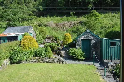 a garden with a small shed and a stone wall at Tre-Allt Gorgeous Cottage in Dolgellau