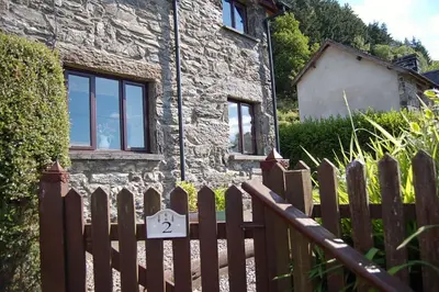 a wooden fence in front of a stone house at Tre-Allt Gorgeous Cottage in Dolgellau