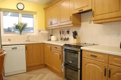 a kitchen with wooden cabinets and a clock on the wall at Wulfrun in Tywyn