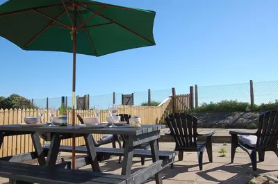 a picnic table with a green umbrella and chairs at Sunny Side Up Beach House in Tywyn in Tywyn