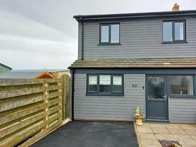 a gray house with a fence and a yellow fire hydrant at Swn Y Tonnau in Tywyn