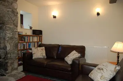 a living room with a brown leather couch and a book shelf at Henborth Mawr Cottage in Talybont in Talybont
