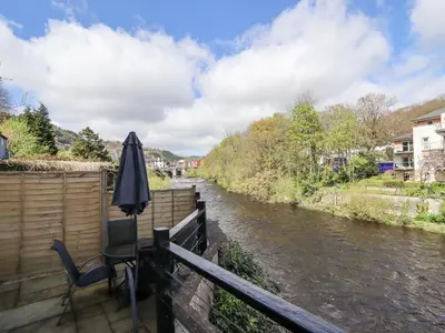 an umbrella and chair sitting on a balcony next to a river at No 9 On The Riverbank in Llangollen