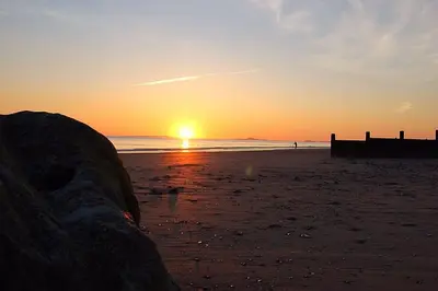a sunset on the beach with the sun setting at Caravan 309 Bryn Y Mor Beach Side Park in Tywyn