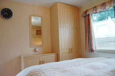 a bedroom with a bed and a mirror and a window at Caravan B26 at The Woodlands in Tywyn