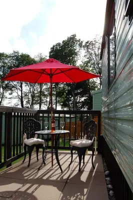 a table and chairs with a red umbrella on a patio at Caravan B26 at The Woodlands in Tywyn