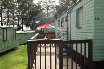 an outdoor deck with a table and an umbrella at Caravan B26 at The Woodlands in Tywyn