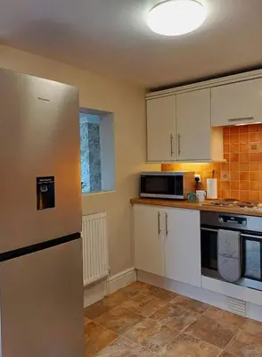 a kitchen with white cabinets and a stainless steel refrigerator at South View Cottage with Terrace and Coastal Views in Fairbourne