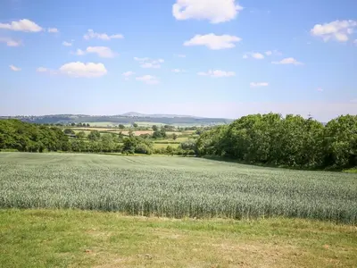 a large field of grass with trees and a blue sky at Finest Retreats - Norton Cottage in Onibury
