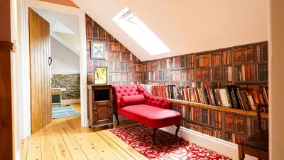 a red chair in front of a library with books at Mwsogl - Luxurious Family Fishing Lodge Near Aberaeron With Private Fishing in Cross Inn