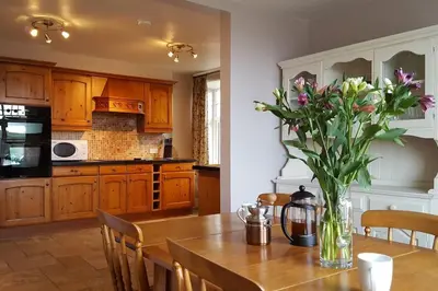 a kitchen with a wooden table with a vase of flowers at Holiday Cottage in Snowdonia (Sleeps 10) in Harlech