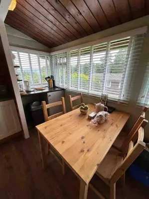a wooden dining table in a kitchen with windows at Snug and cosy log cabin. in Trawsfynydd