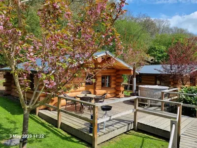 a log cabin with a deck and a tree at Mountain Edge Resort Lodge 2 with Hot Tub in Church Stretton