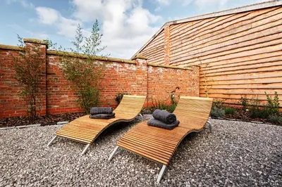 two chairs with pillows sitting next to a brick wall at Pigeon House - Unique Barn with private garden, hot tub and wood burner in Shrewsbury