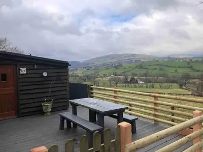 a picnic table on a deck with a view of a hill at The Retreat in Llanrhaeadr-ym-Mochnant