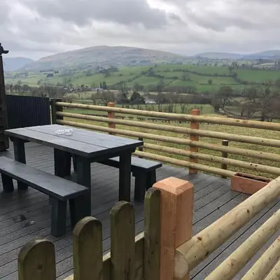 a picnic table and benches on a deck with a view at The Retreat in Llanrhaeadr-ym-Mochnant