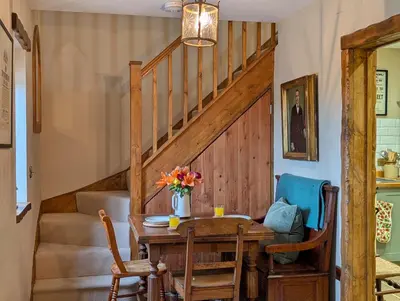 a dining room with a table and a staircase at Romantic Country Cottage with log burner, garden patio, outdoor tub and country views- Brecon Beacons National Park in Llangadog