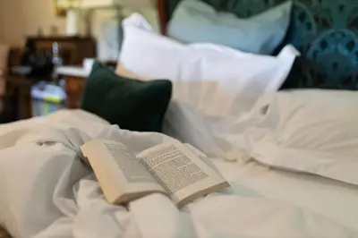 a book laying on top of a bed with pillows at Romantic Country Cottage with log burner, garden patio, outdoor tub and country views- Brecon Beacons National Park in Llangadog