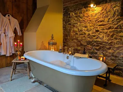 a bath tub in a room with a stone wall at Romantic Country Cottage with log burner, garden patio, outdoor tub and country views- Brecon Beacons National Park in Llangadog