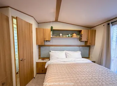 a small bedroom with a bed and wooden cabinets at Little Curlew, Ynyslas, Borth in Borth