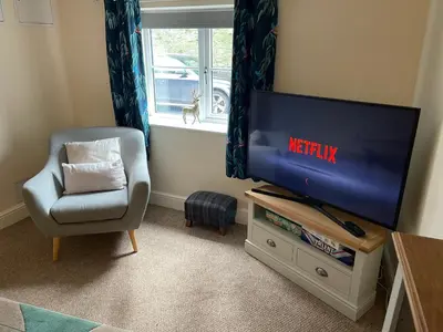 a living room with a tv and a chair and a window at Beech Cottage with Clun Castle View in Clun