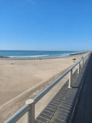 a sandy beach with a metal railing next to the ocean at Glan Y Morfa Bach The Stone Cottage in Tywyn